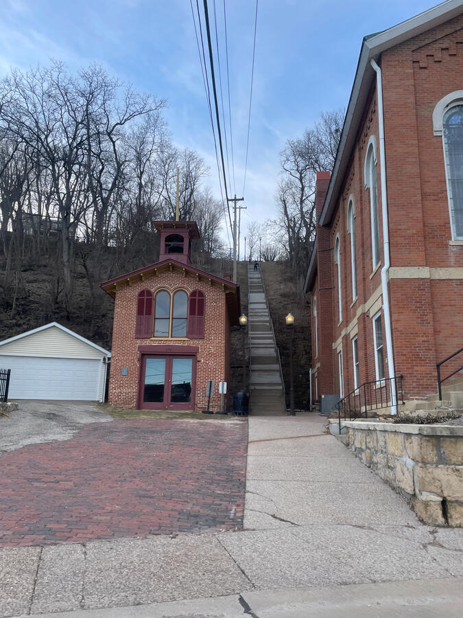 Narrow brick alleyway in Galena, Illinois, showing historic multi‑story brick buildings, a red‑brick street transition, and a small cupola‑topped structure framed by leafless hillside trees under a clear sky.