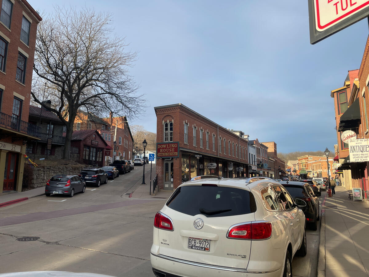 Historic downtown Galena, Illinois, featuring the 19th‑century brick storefronts along a sloped street, including the Dowling House and nearby antique shops, with parked cars and a large leafless tree at the corner.