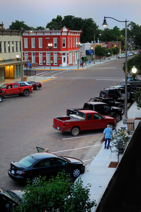 lindsborg-kansas-downtown-evening-lights Evening view of downtown Lindsborg with warm street lighting and parked cars along brick buildings.
