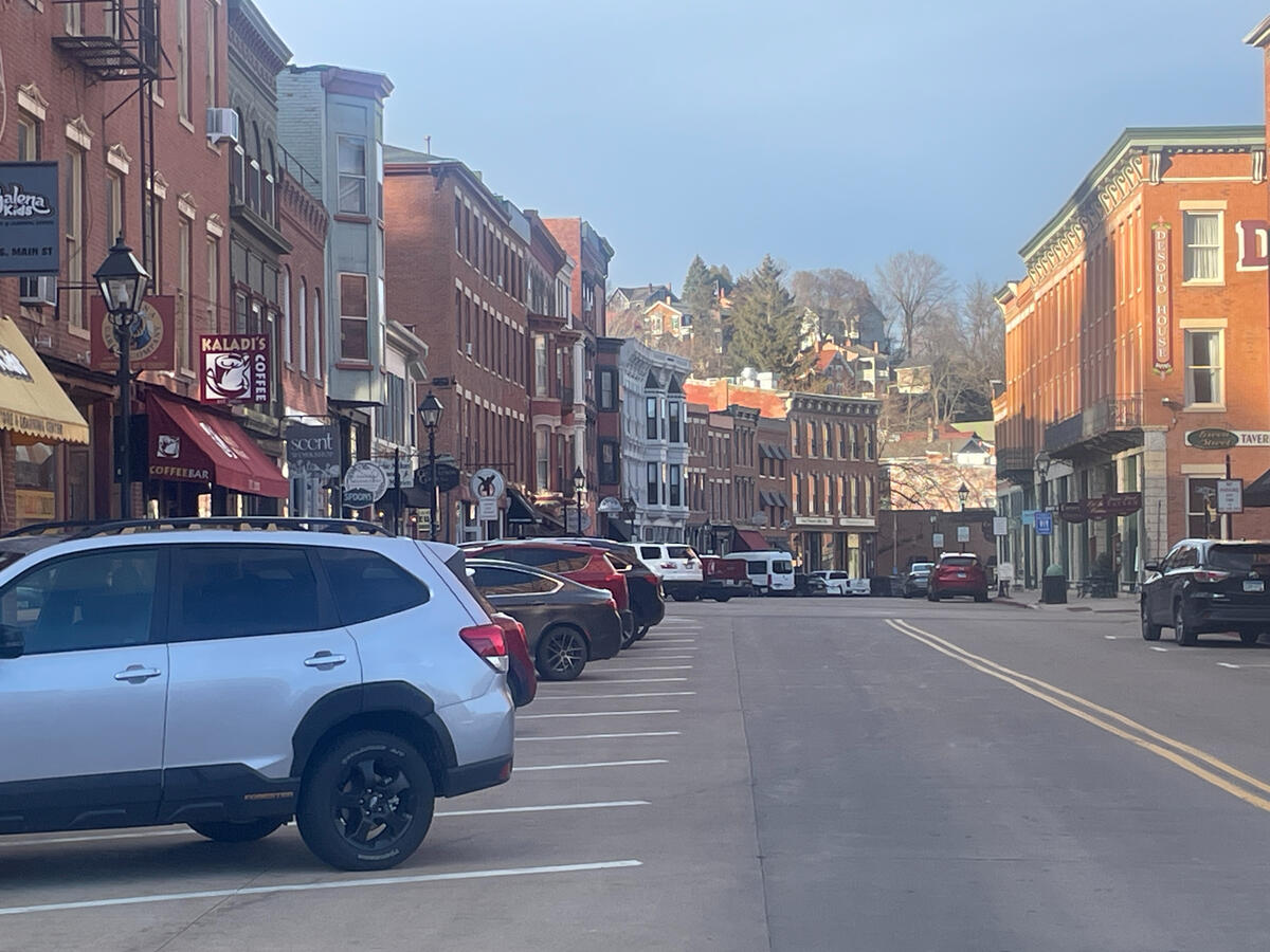 Historic downtown street in Galena, Illinois, featuring 19th‑century brick buildings, local shops like Kaladi’s Coffee and the Desoto House, and parked cars along the quiet roadway on a clear day.