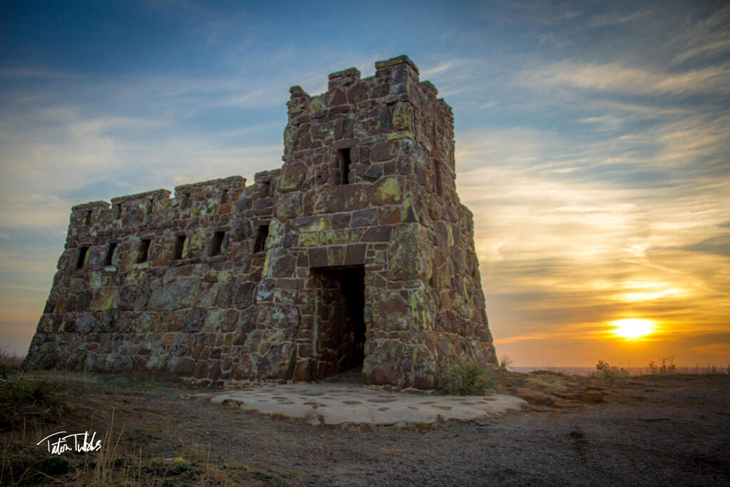 Sunrise at Coronado Heights_Taton Tubbs A stone tower at Coronado Heights in Lindsborg, Kansas, lit by warm sunrise light with a colorful sky and the sun low on the horizon.