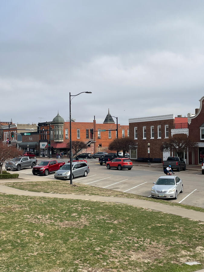 Downtown Pella street scene with storefronts, brick sidewalks, and parked cars.