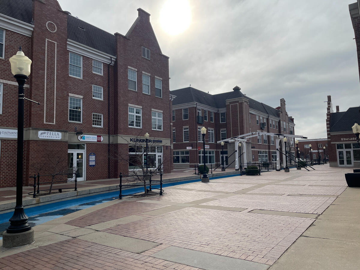 Molengracht canal with brick plaza, benches, and Dutch‑inspired mixed‑use buildings.
