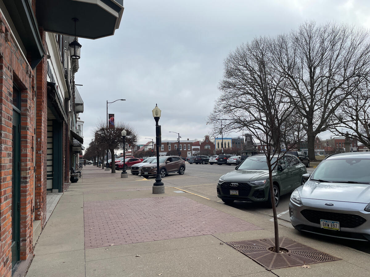 Quiet downtown Pella street with brick buildings, storefront awnings, and parked cars.