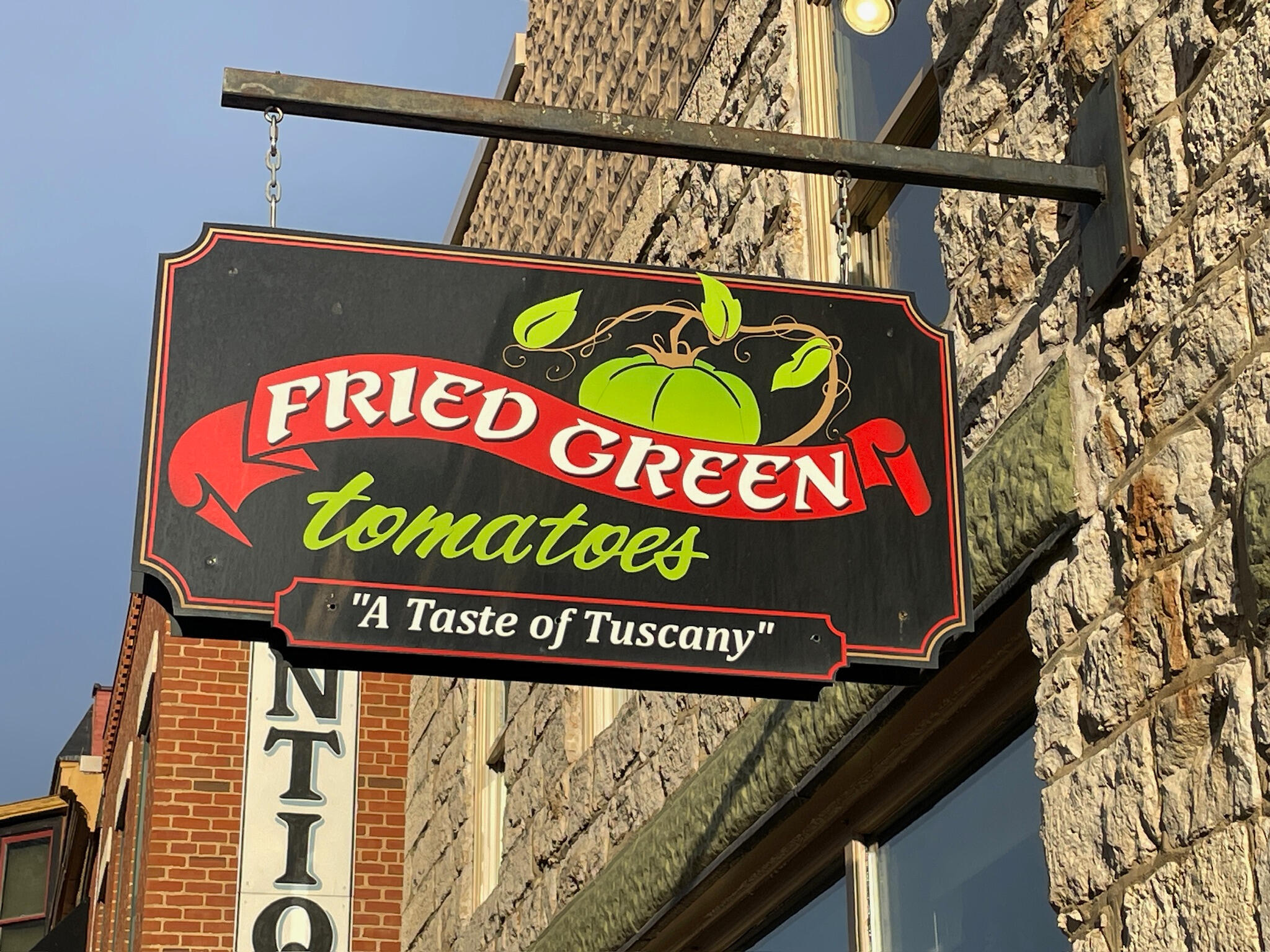 Vintage-style wooden restaurant sign for Fried Green Tomatoes featuring a red banner, green script lettering, and the tagline