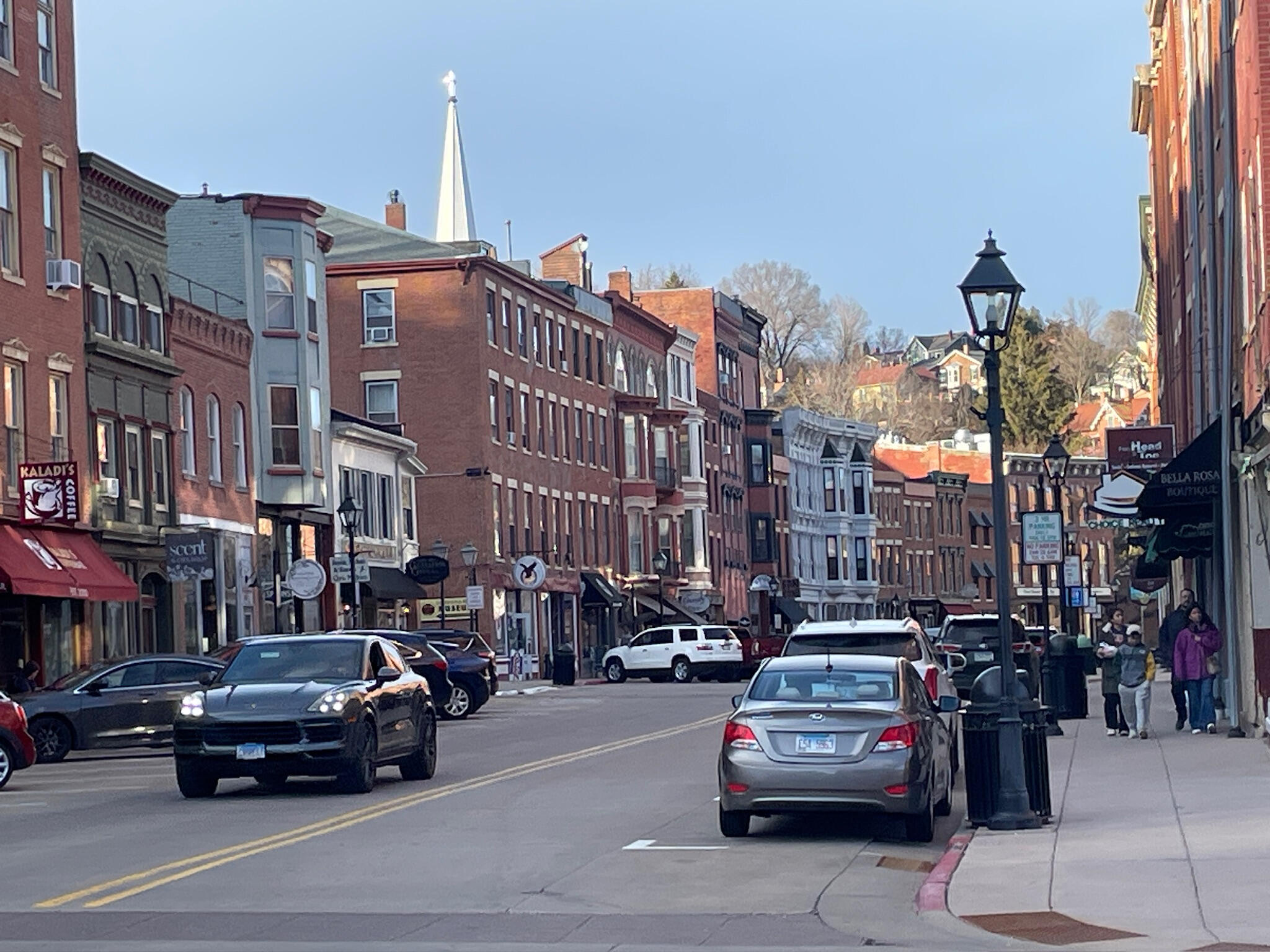Historic Main Street in Galena, Illinois, showing 19th-century red brick buildings, local shops like Kaladi's Coffee, and a church steeple under a clear blue sky.
