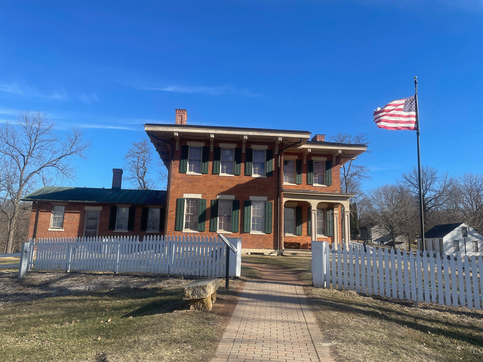 ulysses-s-grant-home-flag-galena-illinois Exterior of the Ulysses S. Grant Home State Historic Site in Galena, Illinois, a two-story red brick Italianate mansion with green shutters and an American flag on a sunny day.