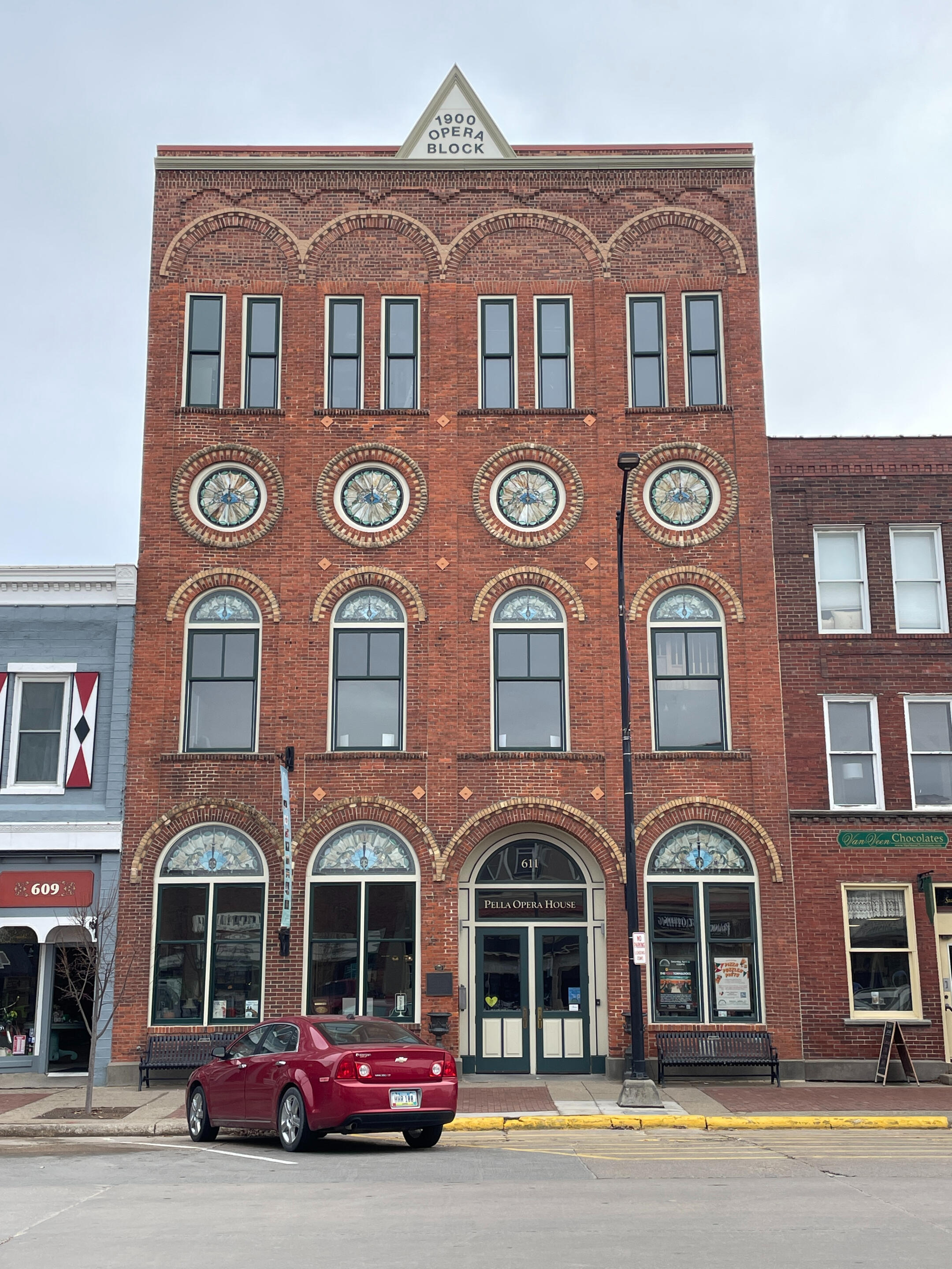 pella-opera-house-historic-building-exterior Historic Pella Opera House with brick detailing, stained-glass accents, and arched ground‑floor entrances.