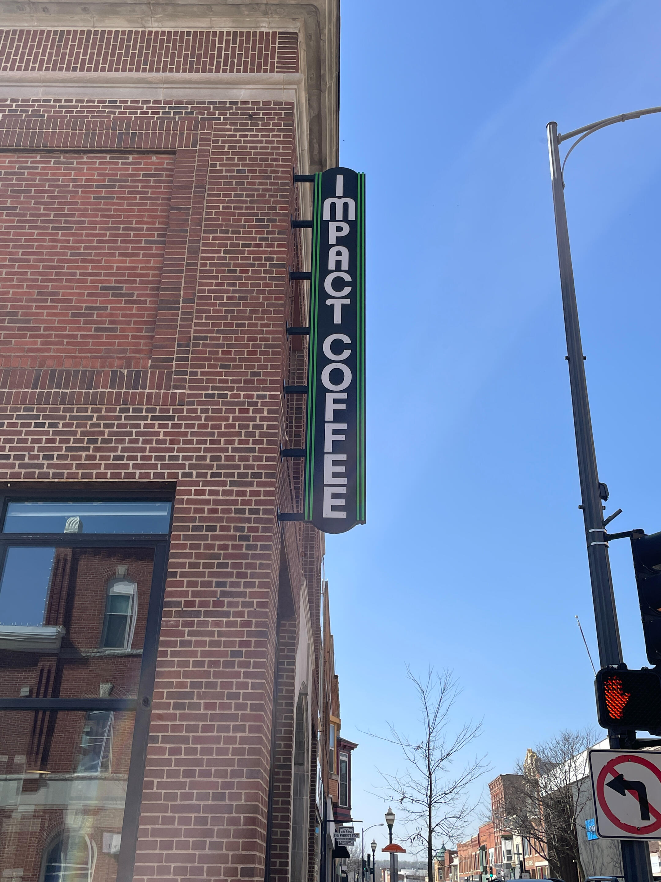Impact Coffee sign on a brick building along a downtown Decorah street under a clear blue sky.