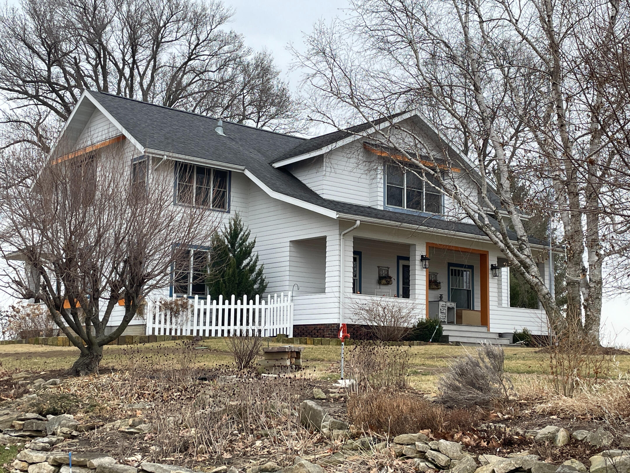 White two‑story Cheesemaker’s Inn with covered porch, dark roof, and winter landscaping.