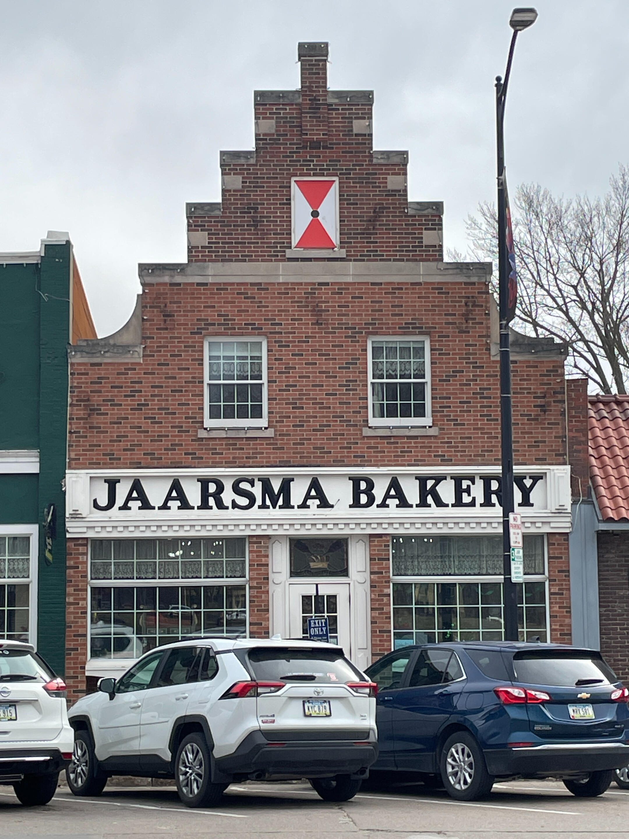 Front of Jaarsma Bakery with its stepped gable façade and street parking in downtown Pella.