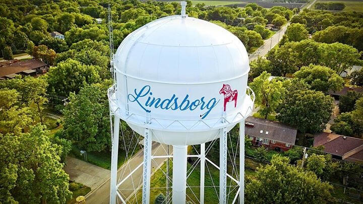 Aerial view of the Lindsborg, Kansas water tower featuring a red Dala horse design, surrounded by treetops and neighborhood streets.